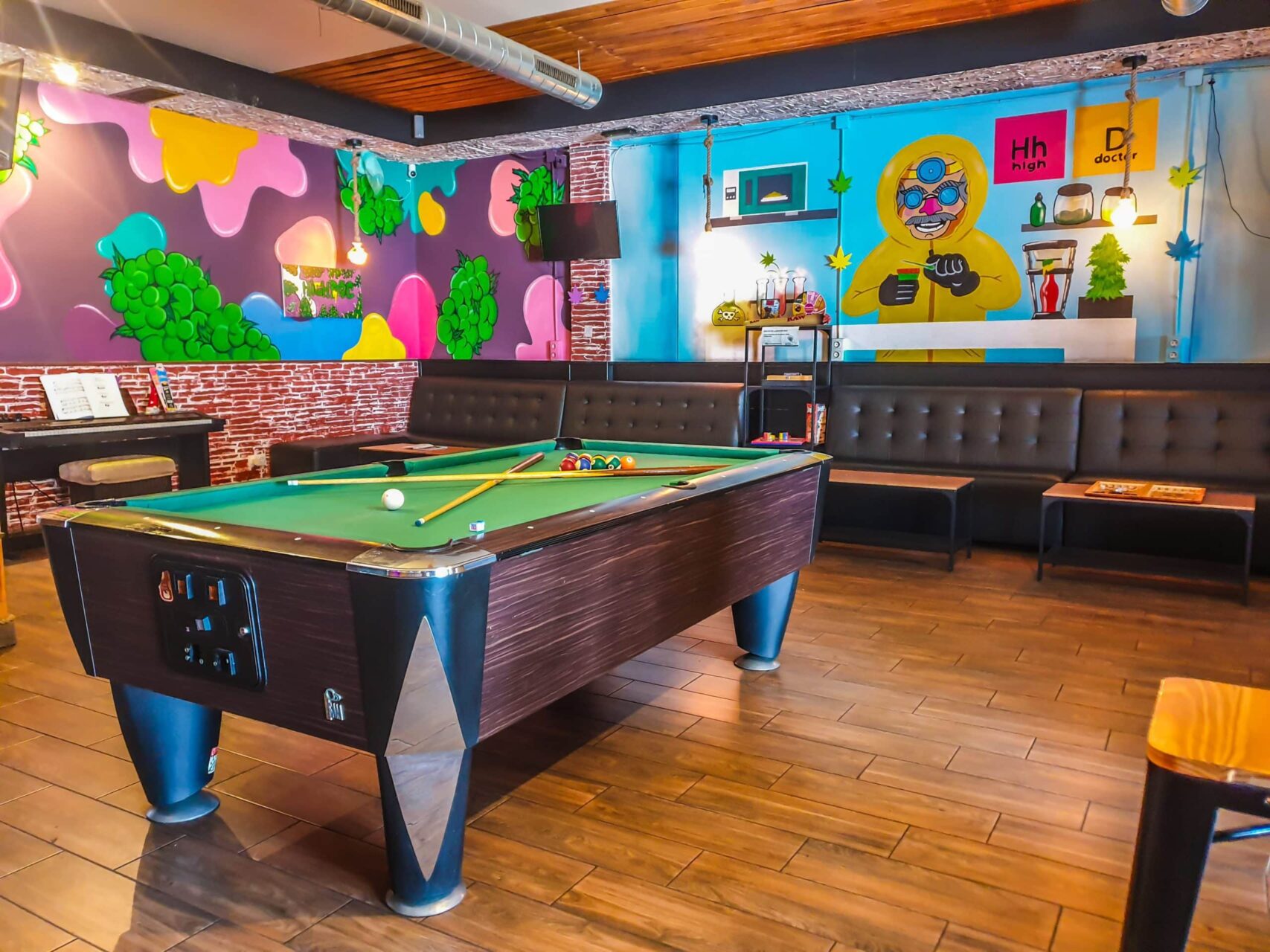 Interior of The High Doctor CSC in Alicante with pool table, long black sofas and colorful graffiti walls.