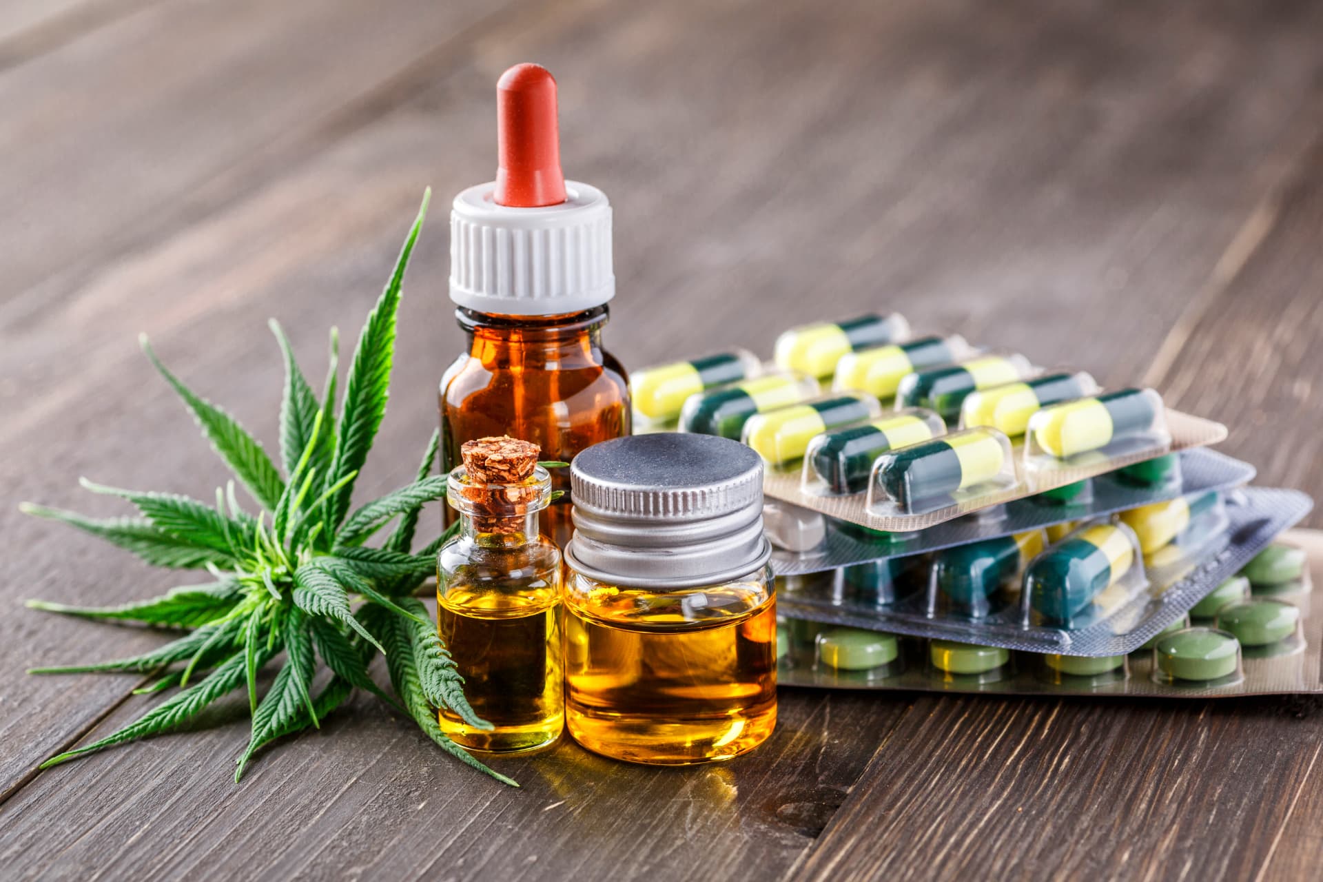 Cannabisblatt, Flaschen mit Cannabisöl und Kapseln auf einem Holztisch