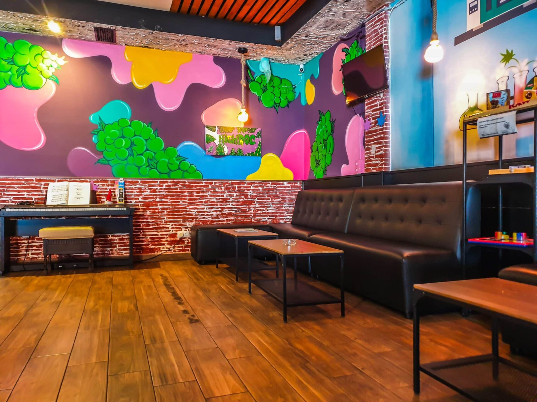 Interior of The High Doctor coffeeshop in Alicante with colorful graffiti walls, black leather sofas and wooden floors.