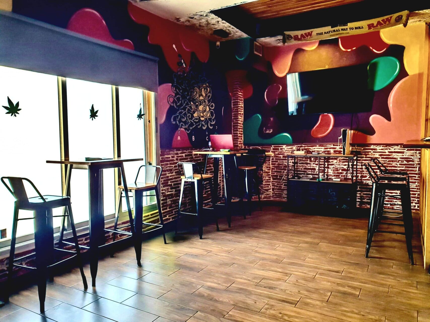 Interior of The High Doctor CSC in Alicante with high tables, metal stools and colorful graffiti wall.