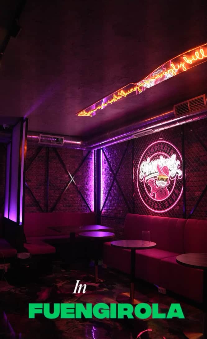 Video preview of Monopoly Social Club in Malaga, lounge with pink ambient lighting, brick wall backdrop, round tables, and pink upholstered sofas.  