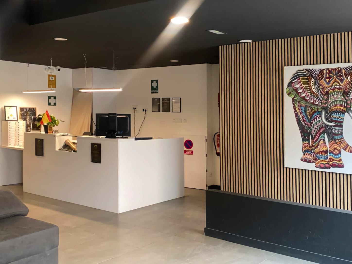 The minimalist white reception desk at Four Twenty cannabis club in Valencia, featuring modern lighting and a colorful elephant painting on a wooden slat wall.