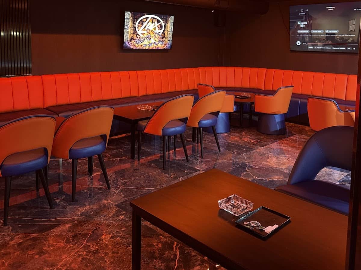 Interior of Lux Lounge social club in Marbella with orange velvet sofas, TV screen and marble floor.