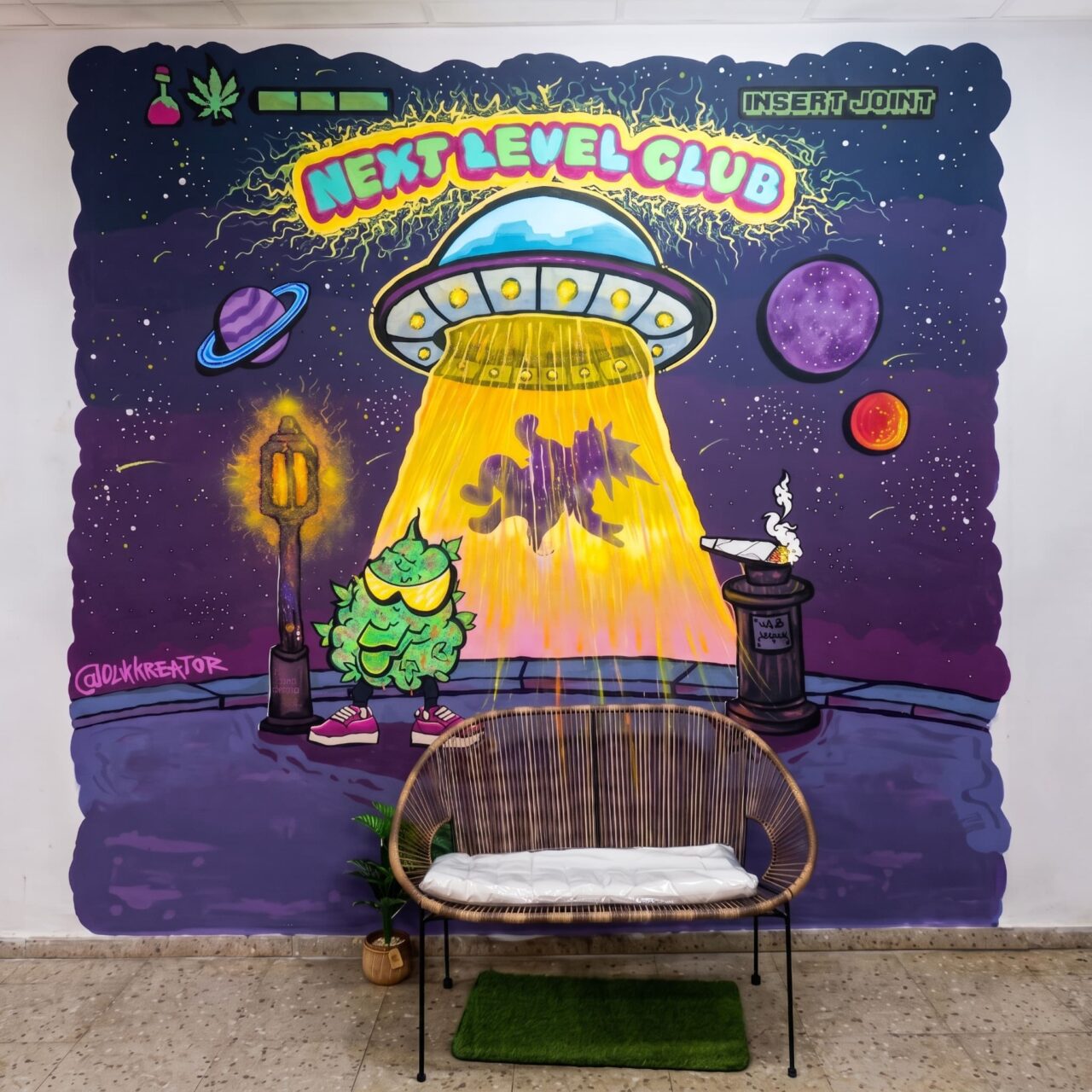 Interior of Next Level Club cannabis club in Valencia: a woven bench in front of UFO-themed graffiti.