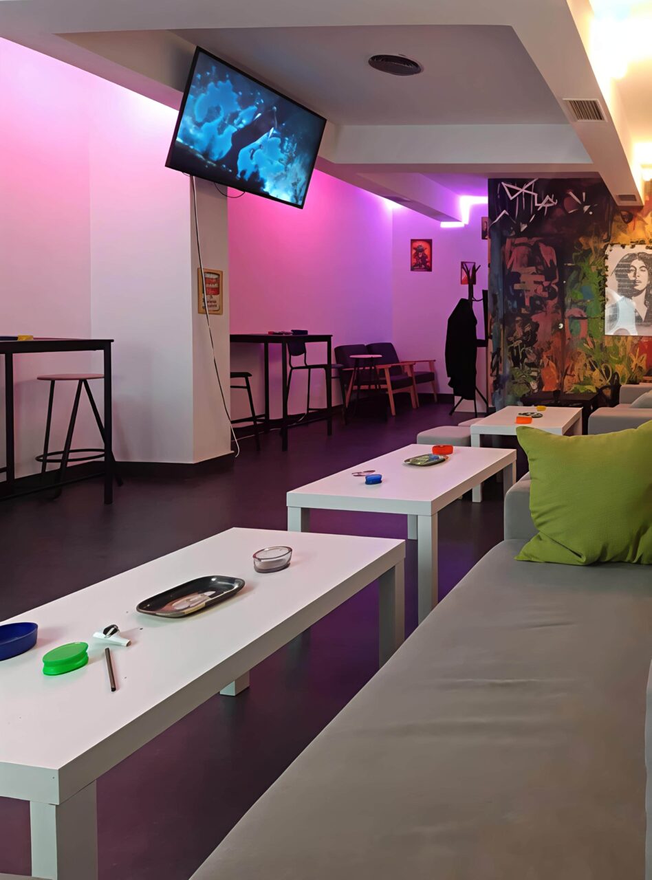Modern lounge interior with purple neon lighting at Valhalla cannabis club in Madrid, featuring low coffee tables, sofas, and bar seating.